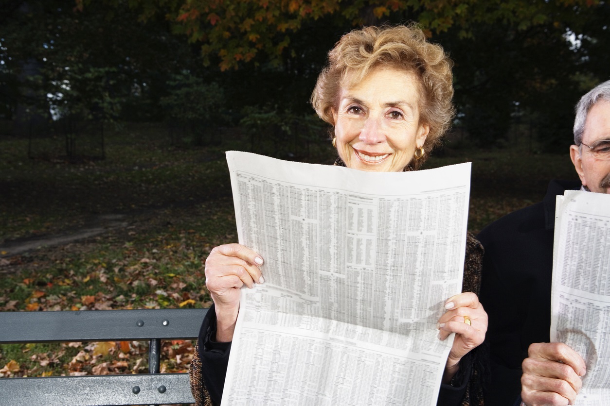 Senior couple reading newspapers on bench outdoors